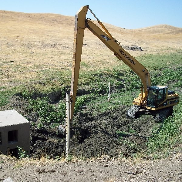 Excavator working at a stream channel beside a gauge house