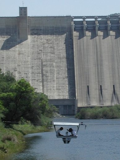 Hydrographers measuring flow from a cableway car below a dam